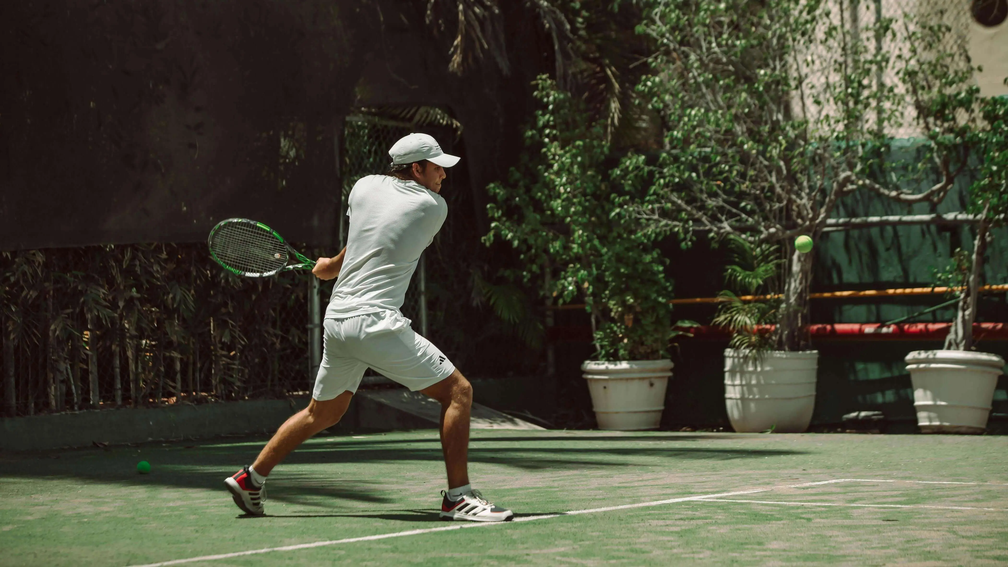 Tennis player hitting a backhand on a green court, demonstrating the techniques and form achieved through Evolve's science based tennis training and comprehensive tennis player development.