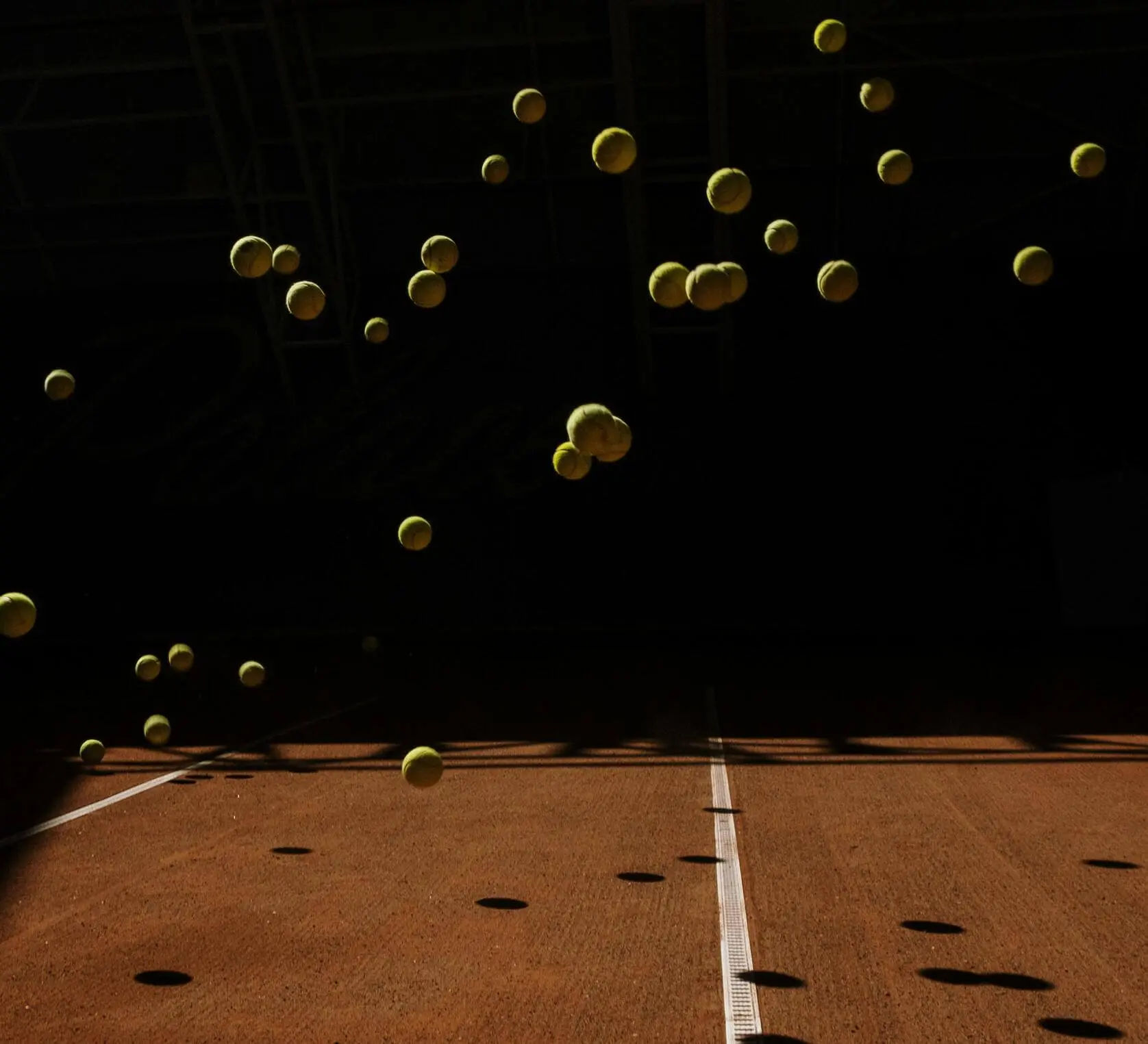 Many tennis balls in the air over a court, symbolizing focused practice and the volume of work in a tennis fitness routine and full body tennis workout guided by our online tennis program.