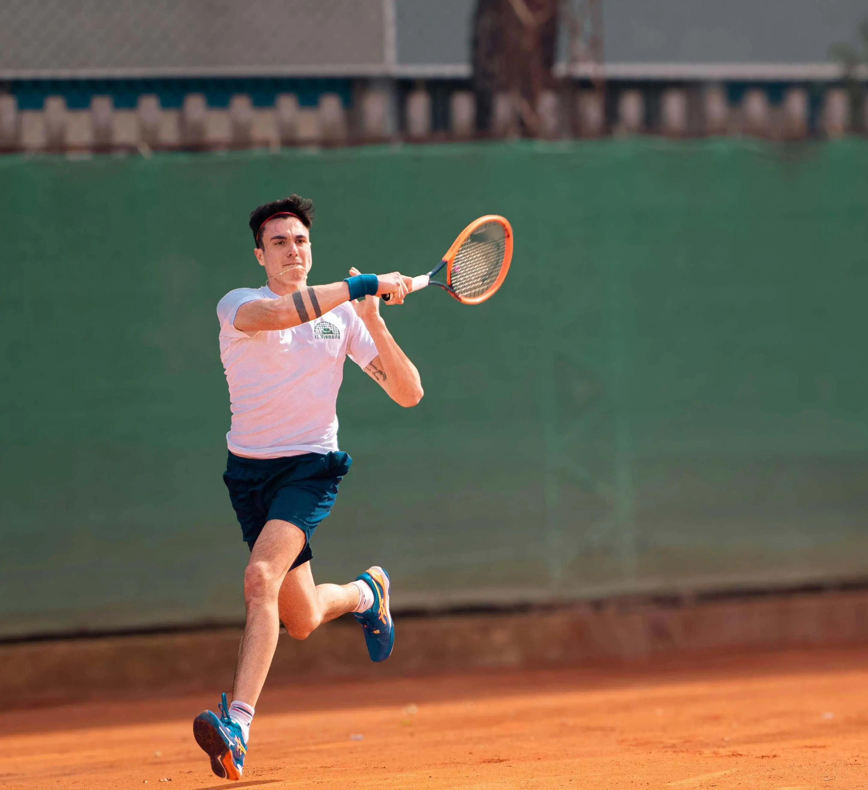 Male tennis player hitting a powerful forehand on a clay court, demonstrating the results of science based tennis training within an Evolve adult tennis program or tennis high performance camp.