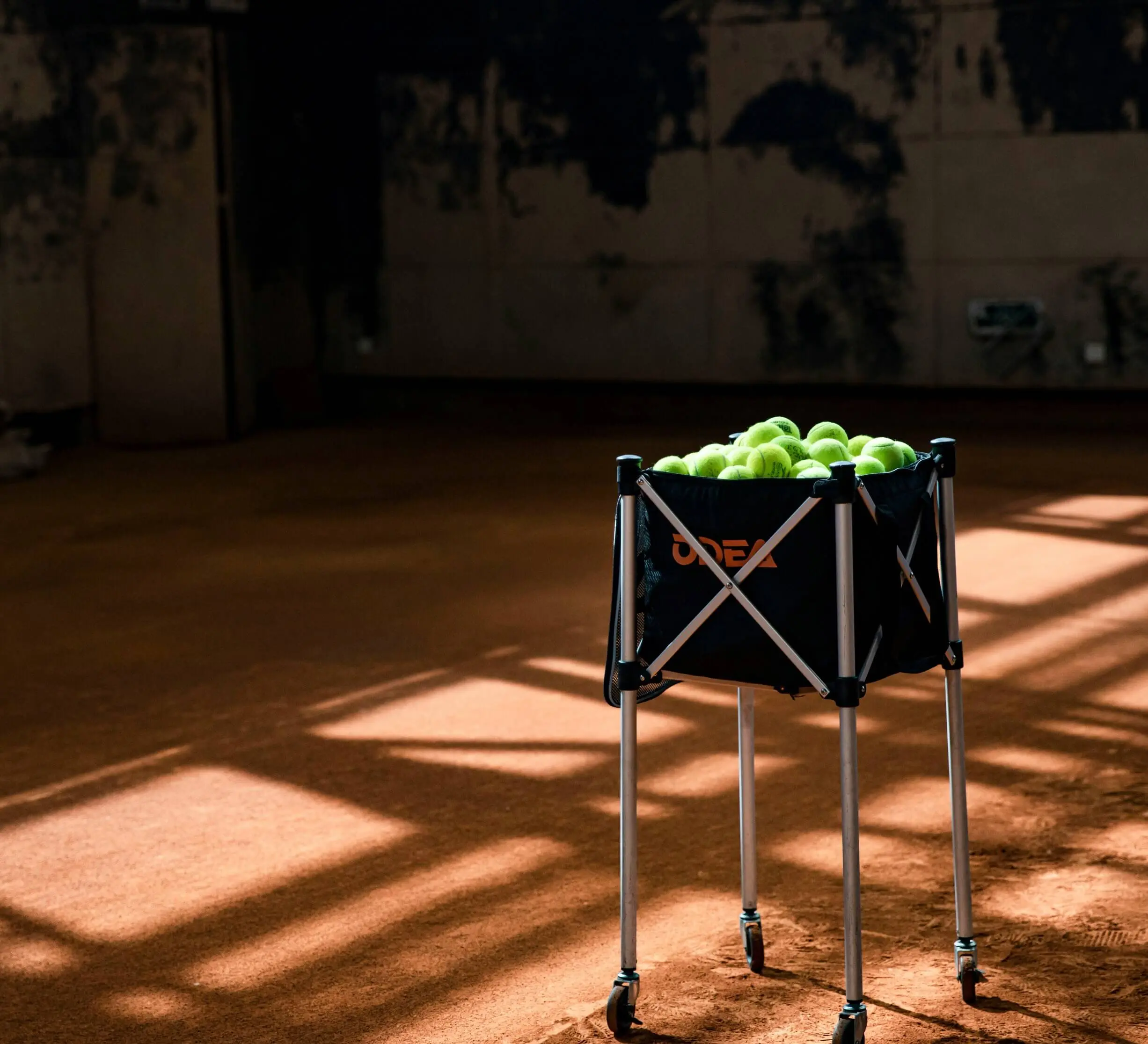 A basket of tennis balls on a clay court, symbolizing the essential tools used in Evolve's science based tennis training and the practical process of how to develop a tennis player.