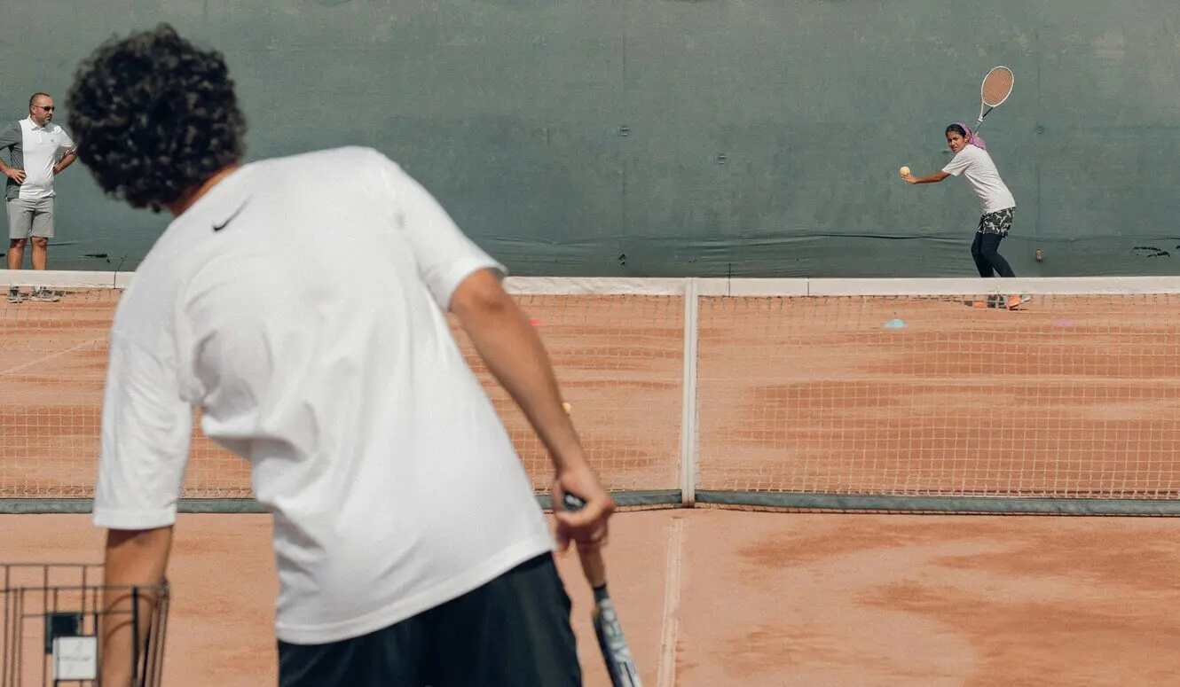 Coach observing players on a tennis court, representing the ongoing guidance and expertise provided for tennis coach development and enhancing tennis club development through quality coaching.