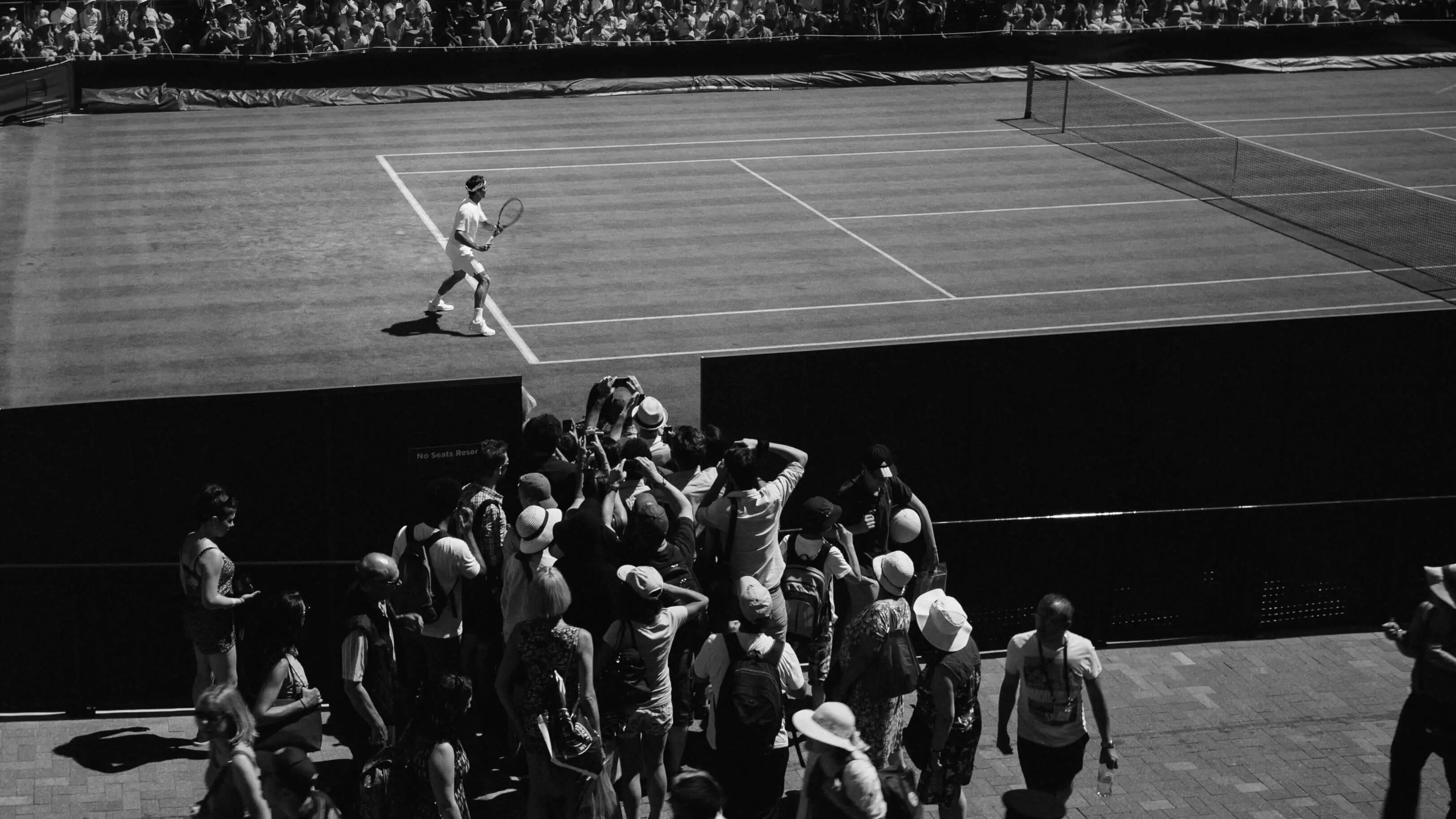 Black and white photo of a tennis player on a grand court with a crowd watching, symbolizing the aspirations and professional tennis player development plan fostered by Evolve's programs.
